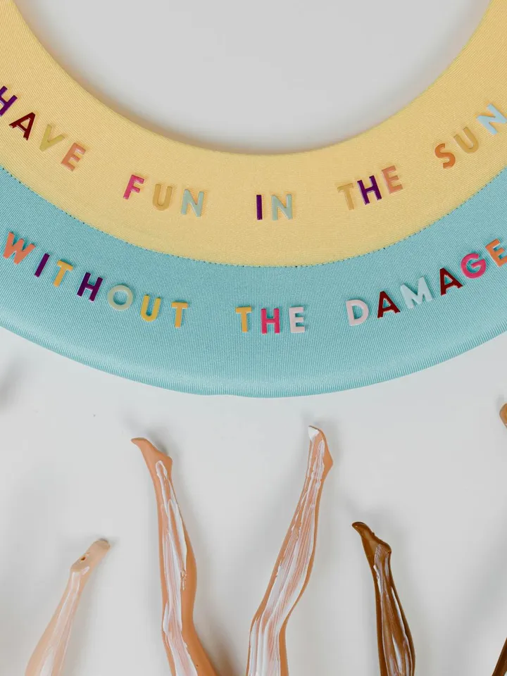 Colorful circular plates with the text 'Have fun in the sun without the damage' around the edge, and several dollops of sunscreen drips at the bottom.