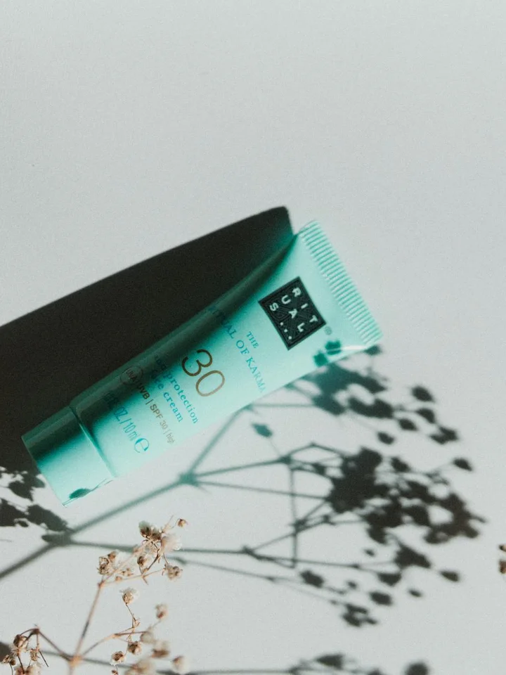 Turquoise sunscreen tube labeled SPF 30 lying diagonally with plant shadows on a light background.