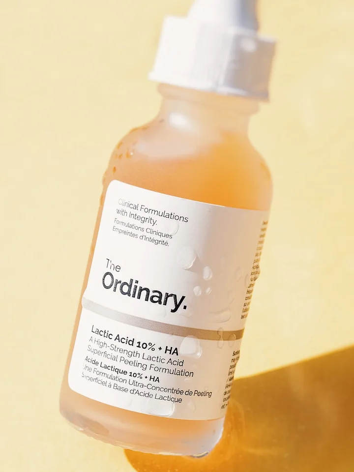 Close-up of The Ordinary Lactic Acid 10% + HA serum bottle against a warm yellow background.