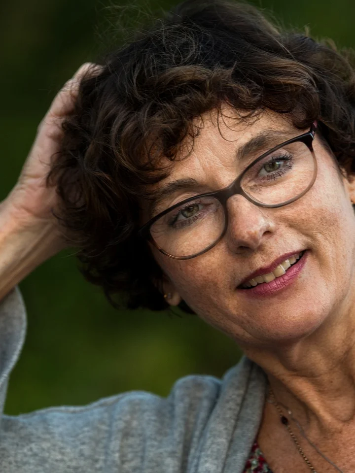 Portrait of a middle-aged woman with short curly hair and glasses, outdoors.