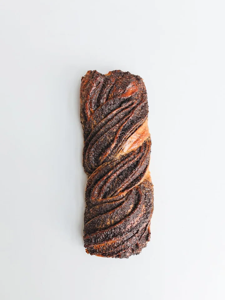 Close-up of a twisted, dark-brown pastry on a clean white surface