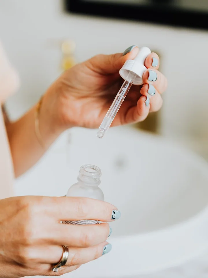 Hands holding a dropper bottle of vitamin C serum over a small bottle, ready to apply