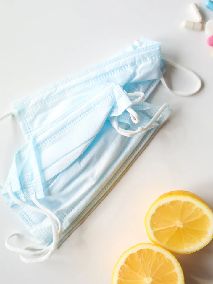 Blue disposable surgical mask on a white surface with lemon halves nearby