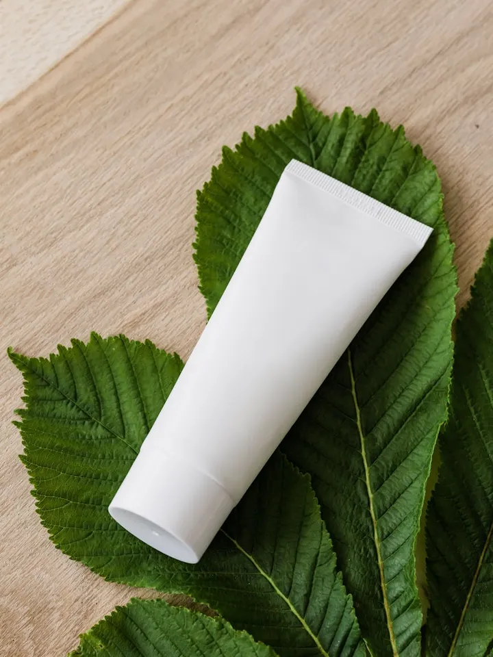 White cosmetic tube diagonally placed on large green leaves on a wooden surface.