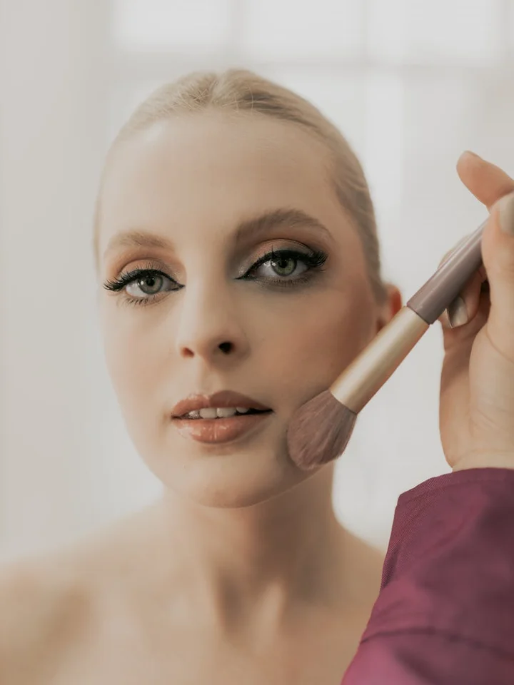 Close-up of a woman applying foundation with a makeup brush on her cheek, showcasing smooth, non-comedogenic coverage.