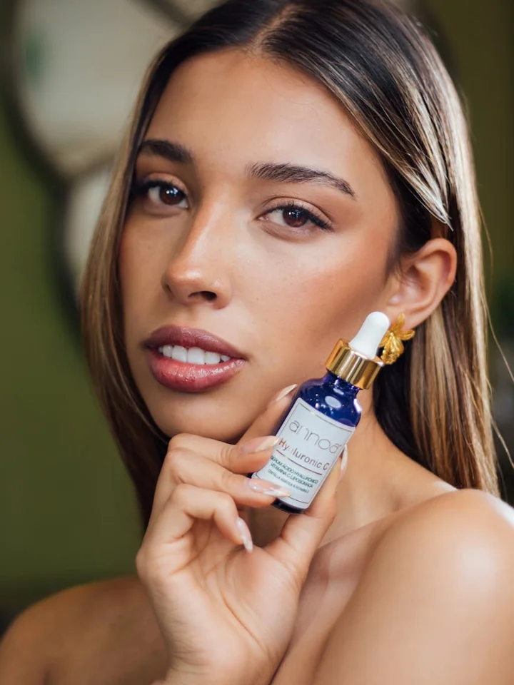 Close-up of a woman holding a blue serum dropper bottle with a gold cap.